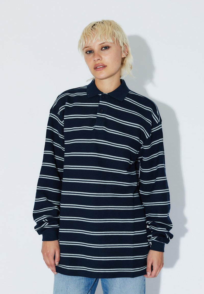 Polo a maniche lunghe blu navy con righe orizzontali bianche, dotato di colletto con bottoni e vestibilità comoda. Materiale in cotone morbido.