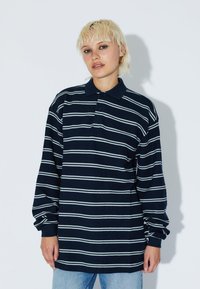 Navy long-sleeve polo shirt with white stripes, features a collared neckline and button placket. Cotton blend fabric, relaxed fit design.