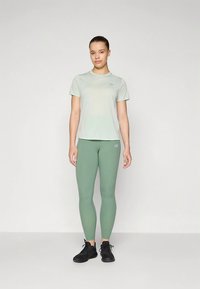 Light green athletic t-shirt paired with fitted green leggings, both made of smooth, breathable fabric. Black athletic shoes complete the outfit.