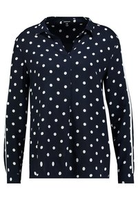 Camicia azzurra con bottoni, a pois bianchi, maniche lunghe e colletto a punta; presenta righe bianche lungo le maniche.