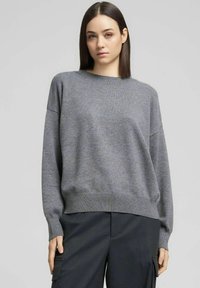 Maglione grigio lavorato a maglia con scollo rotondo, spalle scivolate e orlo a coste. Il tessuto è morbido con una texture liscia e vestibilità rilassata.