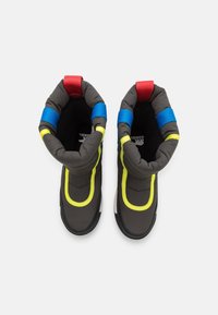 Botas aislantes negras con parte superior acolchada, correas de tela en colores azul y rojo, y acentos en amarillo neón. Suela de goma y forma redondeada.