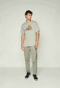 Graues Grafik-T-Shirt mit einem bunten urbanen Design, kombiniert mit hellgrauen Jogginghosen mit schwarzen Seitenstreifen und schwarzen Sneakers.