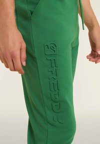 Pantaloni di felpa verde in cotone con tasche laterali e logo "FREDDY" in rilievo. Presentano un elastico in vita con cordino e una texture liscia.