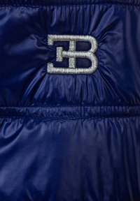Giacca in nylon blu con orlo elastico, caratterizzata da un logo ricamato in argento "EB" nella zona del petto, che mette in risalto una texture liscia e lucida.