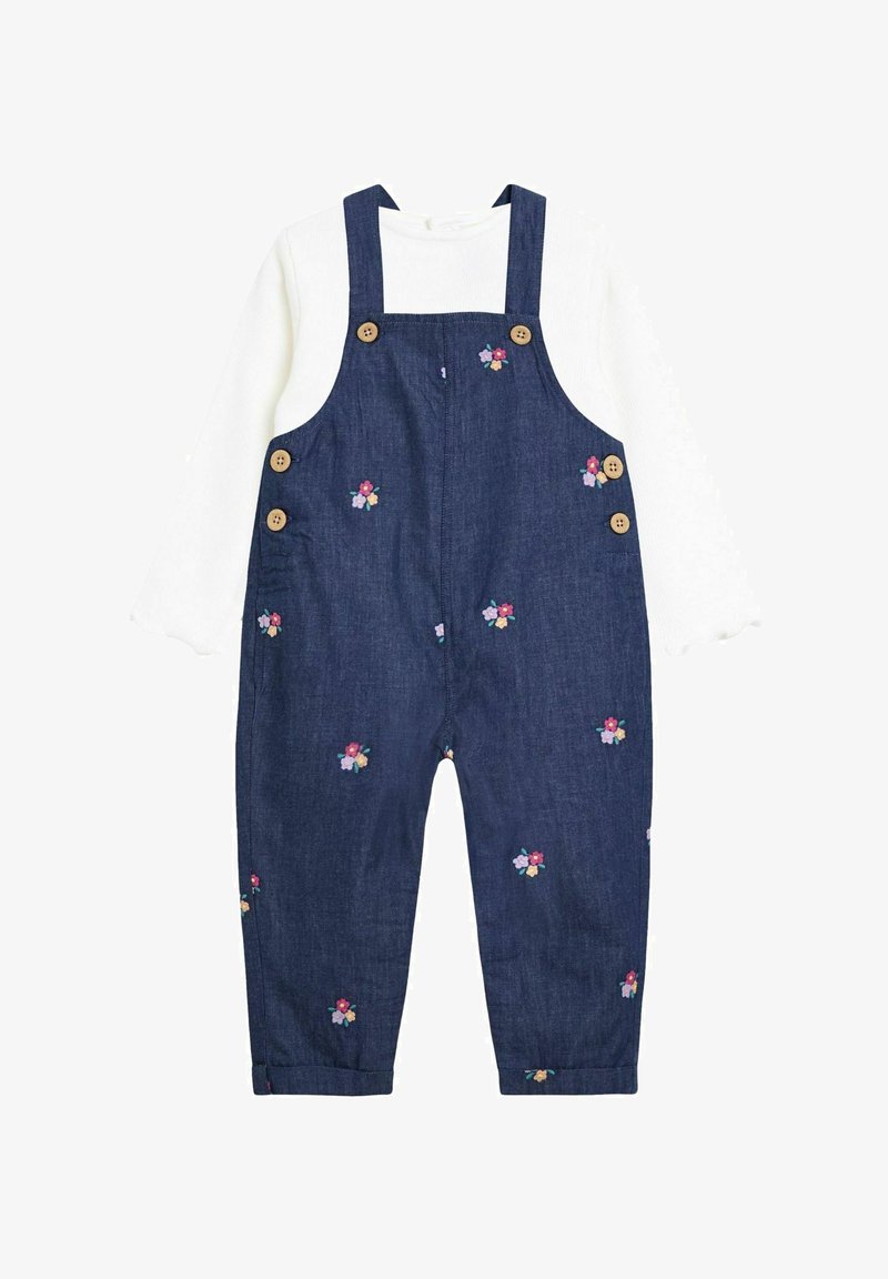 Baltas ilgomis rankovėmis marškinis, derinamas su tamsiai mėlynomis džinsinėmis kombinezonėmis, puoštomis mažomis gėlių siuvinėjimais ir rudos spalvos mygtukais ant petnešų ir šonų.