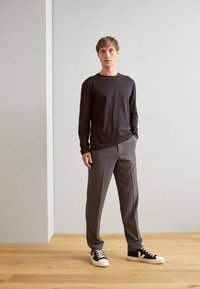 Schwarzes Langarmhemd, graue maßgeschneiderte Hosen und schwarze Sneakers mit weißen Akzenten. Glatte Textur, taillierte Passform und minimalistischer Stil.