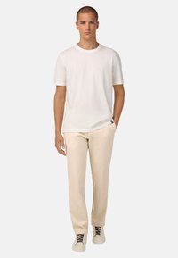 Vyrų balta medvilninė marškinėlių viršūnė su apvali iškirpte, derinama su smėlio spalvos kelnėmis ir šviesiais sportbačiais su juodais raišteliais. Paprastas ir modernus siluetas.