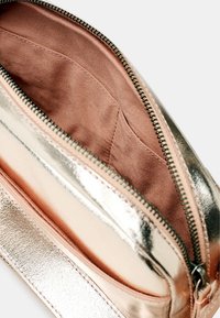 Borsa cosmetica metallica dorata con superficie liscia, chiusura a zip e rivestimento interno in satin rosa. Internamente presenta un compartimento per l'organizzazione.