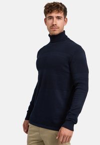 Marineblå strikket høyhalset genser med teksturerte horisontale striper, en tettsittende silhuett og ribbede mansjetter. Laget av mykt, pustende materiale.