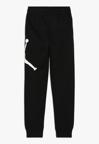 Pantalones de chándal de algodón negros con cintura y puños elásticos, que presentan un gran logo Jumpman blanco en la pierna izquierda.