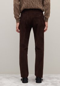 Pantalones de pana marrón con corte recto, con una superficie acanalada y texturizada, dos bolsillos traseros y zapatos negros.