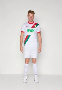Camiseta de fútbol blanca con rayas diagonales rojas y verdes; logo "WWK" en verde en el pecho; combinada con pantalones cortos y medias blancas.