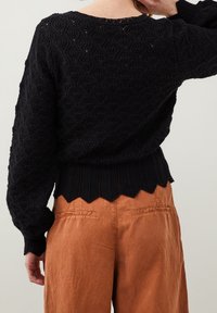 Czarny dziany sweter z teksturowanymi wzorami w kształcie diamentu, szerokimi rękawami i falowanym dołem, zestawiony z wysokim stanem w kolorze rdzy.