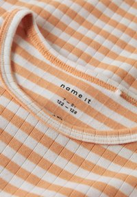 Trumpas rankovėmis, campaigning T-shirt su pakaitinėmis oranžinėmis ir baltomis juostelėmis. Apvalus kaklas, su ženklu ir dydžio etikete vidinėje apykaklėje.