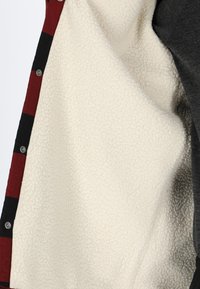 Fleece-gevoerde jas met een rood en zwart geruit buitenstof. Voorzien van zilveren drukknoopjes en een zachte witte binnenvoering.