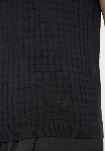 Tmavo modrý pletený sveter s mriežkovým vzorom, ktorý má textúrovaný povrch a rebrovaný spodný okraj. Vyrobený z jemného, flexibilného materiálu.