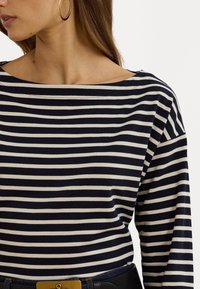 Blusa de rayas en azul marino y crema de manga larga con escote barco, hecha de una tela suave, que presenta un corte relajado y un sutil detalle de costura.