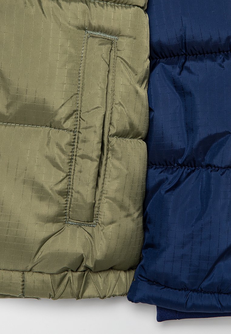 Primer plano de las mangas de una chaqueta de plumas acolchada en verde y azul marino, con costuras visibles y textura acolchada.