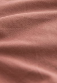 Țesătură de bumbac moale, terracotta, cu o textură netedă, ușor nervurată, având umbre subtile de la straturi pliate.