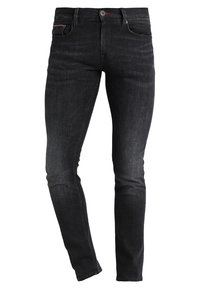 Jeans negros de denim ajustados con una textura ligeramente desgastada. Las características incluyen un cierre de botón, un diseño de cinco bolsillos y costuras en contraste.