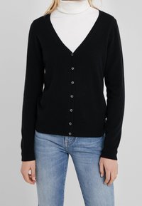 Cardigan nero con scollo a V e maniche lunghe, caratterizzato da bottoni evidenti sul davanti. Materiale a maglia morbido con uno stile aderente.