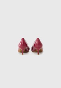 Scarpe con tacco alto in pelle rossa con punta affusolata e tacco sottile, che mostrano una texture liscia e un design minimalista.