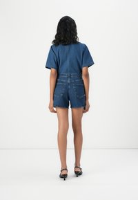 Denim jumpsuit with short sleeves, belted waist, and back pockets. Dark blue color; smooth texture; fitted design, ending above the knee.