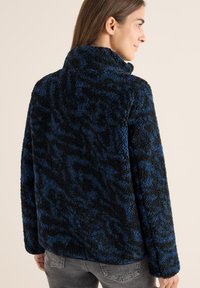 Giacca in pelliccia sintetica nera e blu con colletto alto e vestibilità oversize, caratterizzata da una superficie testurizzata e maniche lunghe.