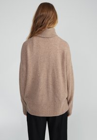 Beige oversized Rollkragenpullover aus weichem Strickmaterial, mit gerippten Bündchen und Saum, entspanntem Schnitt und subtiler Textur.