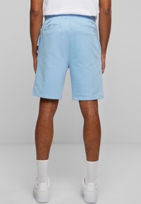 Shorts de sudadera azul claro hechos de un tejido suave, con un corte relajado, cinturilla elástica y dos bolsillos traseros. Zapatillas blancas visibles por debajo.