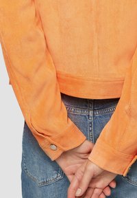 Oranje corduroy jas met lange mouwen en knoopmanchetten, een cropped ontwerp en een gestructureerde afwerking. Gecombineerd met hoge taille denim.