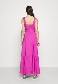 Pitkä vaaleanpunainen puuvillamekko, jossa on kerroksittainen helma, leveät olkaimet ja vartalonmyötäinen yläosa. Takana vetoketjusuljenta, yhdistetty raidallisiin korkokenkiin.