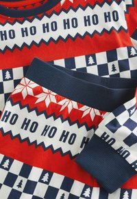 Röd och marinblå mönstrad festväv med upprepande texten "HO HO HO", zigzag-mönster och vintermotiv som träd och snöflingor.