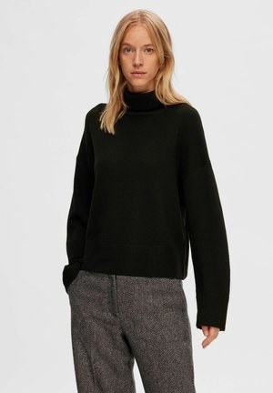 Maglione a collo alto verde scuro con una vestibilità comoda, spalle scese e polsini a coste. Abbinato a pantaloni grigi a scacchi con motivo houndstooth.