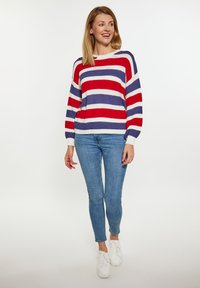 Sweter w paski z dzianiny w kolorach czerwonym, białym i niebieskim; szerokie dekolt i rękawy typu balon; połączony z niebieskimi dżinsami i białymi sneakerami.