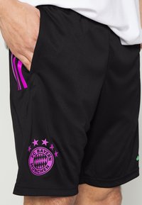 Pantaloni corti del FC Bayern München, realizzati in tessuto nero, presentano un logo rosa con stelle, tasche laterali e dettagli viola sulla vita.