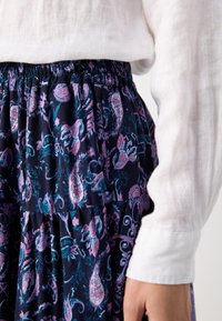 Jupe marine avec un motif paisley en rose et turquoise, dotée d'une taille élastique et d'un design à volants, associée à une chemise à manches longues blanche.