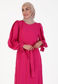 Long pink dress made of lightweight fabric, featuring puff sleeves and a waist tie. Smooth texture with elastic accents at sleeve cuffs.