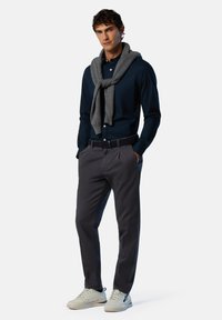Camisa de botones azul marino, bufanda de lana gris drapeada alrededor del cuello, chinos grises y zapatillas ligeras con suelas texturizadas. Luce limpio y moderno.