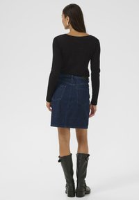 Zwarte langemouwtop gecombineerd met een donkere denimrok. De outfit heeft een eenvoudig ontwerp, met zakken en een rechte pasvorm, aangevuld met zwarte laarzen tot de knie.