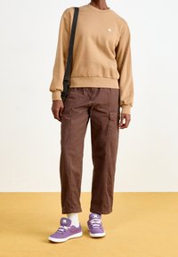 Hnědé bavlněné cargo kalhoty, béžová mikina s malým logem a fialové sneakers. Vlastnosti zahrnují volný střih a pružné manžety.