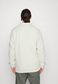 Ljusgrå fleecejacka med krage och långa ärmar. Har en avslappnad passform och mjuk textur, sedd bakifrån.