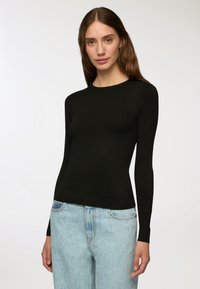 Czarny sweter z długim rękawem i okrągłym dekoltem, wykonany z gładkiego materiału. Dopasowany krój z prążkowanymi wykończeniami przy mankietach i u dołu.