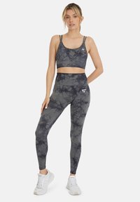 Sportbeha en legging set in een donkergrijze tie-dye patroon, met een aansluitend ontwerp, verstelbare banden en een logo-detail op de leggings.