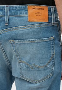 Μπλε τζιν παντελόνι με δερμάτινο ταμπελάκι με την επιγραφή "JACK & JONES." Διαθέτει ραφές στην πίσω τσέπη και ξεθωριασμένο φινίρισμα.