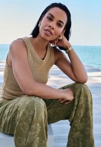 Haut sans manches côtelé couleur fauve avec un décolleté en V, associé à un pantalon large kaki orné d'un motif discret de feuilles. Accessoires en bois tigré.