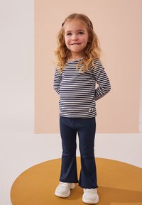 Camiseta de manga larga a rayas azul marino y blanca, leggings acampanados azul oscuro, zapatillas blancas, cabello adornado con clips, sobre un fondo pastel.