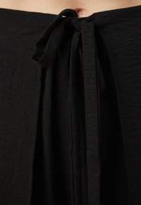 Black fabric with a crinkled texture, featuring a front tie detail at the waist and a flowing design.