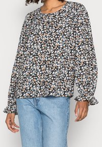 Svart blommig blus med långa, puffiga ärmar och rund halsringning. Har en mix av små blå och persikofärgade blommor på en mörk bakgrund.